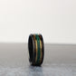 A men’s wedding ring crafted from black tungsten. The design showcases an earthy whiskey barrel wood inlay, accented by a vivid malachite center line and framed with polished yellow gold details.