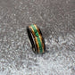 A sleek black tungsten ring with a whiskey barrel wood inlay. The band highlights a bright green malachite stripe, bordered on each side by gleaming yellow gold lines for a modern, elegant look.