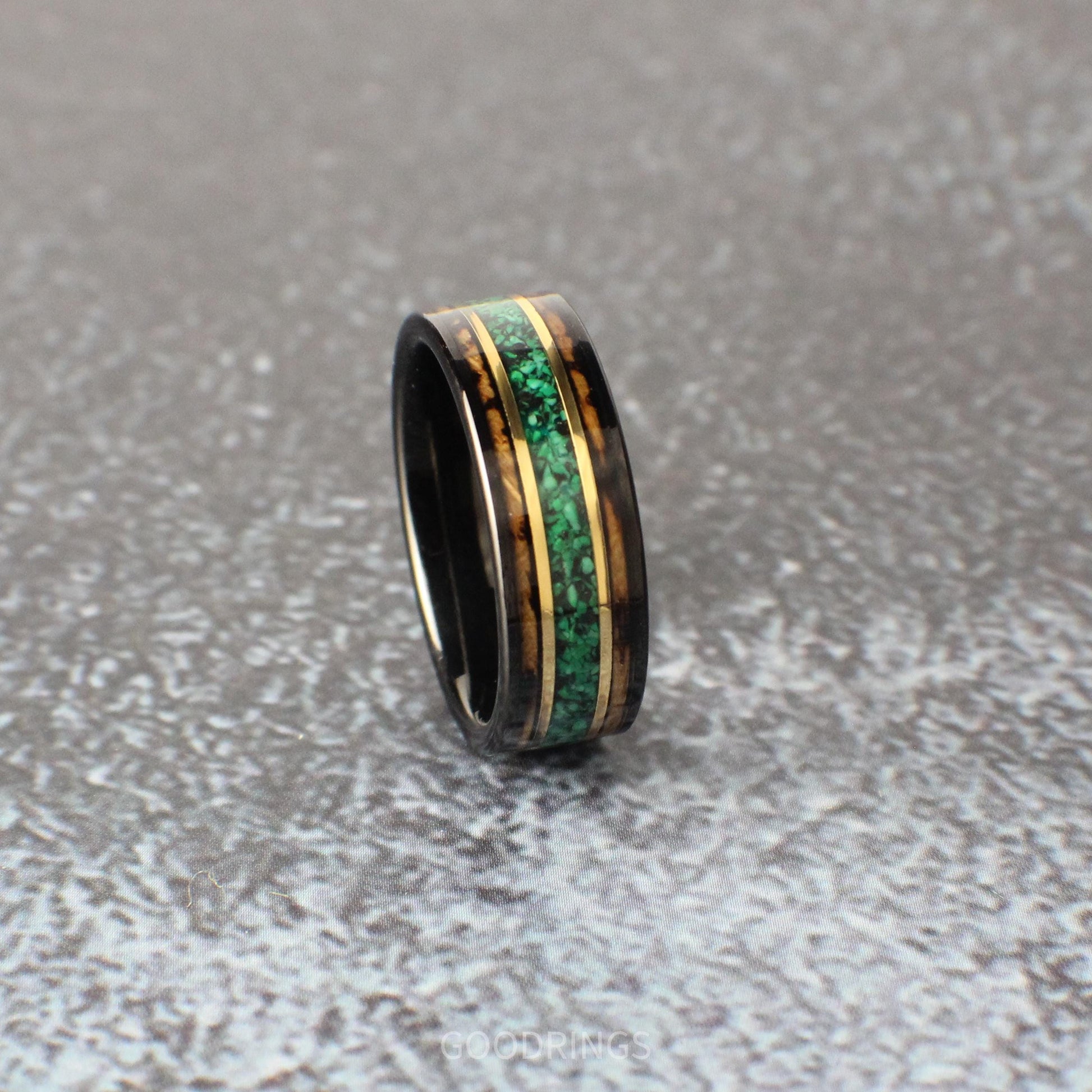 A durable black tungsten men’s band with a whiskey barrel wood inlay. The striking design includes a vibrant malachite center line and two yellow gold accents, blending rustic charm with contemporary sophistication.