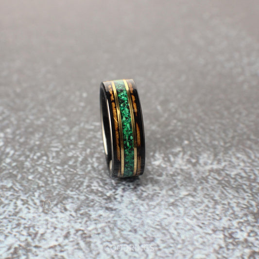 An 8mm wide black tungsten ring featuring a rich whiskey barrel wood inlay. A vibrant green malachite center line is bordered by two narrow bands of yellow gold, adding a bold yet refined touch.